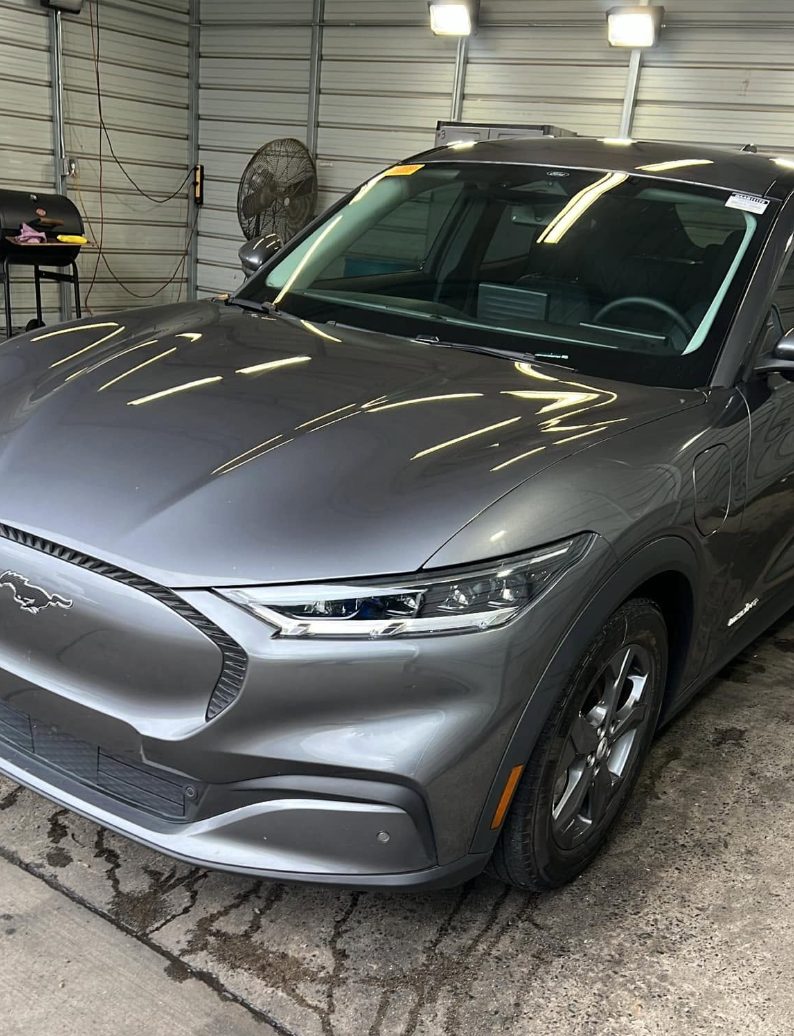 Silver electric Mustang SUV parked in industrial garage with overhead lights