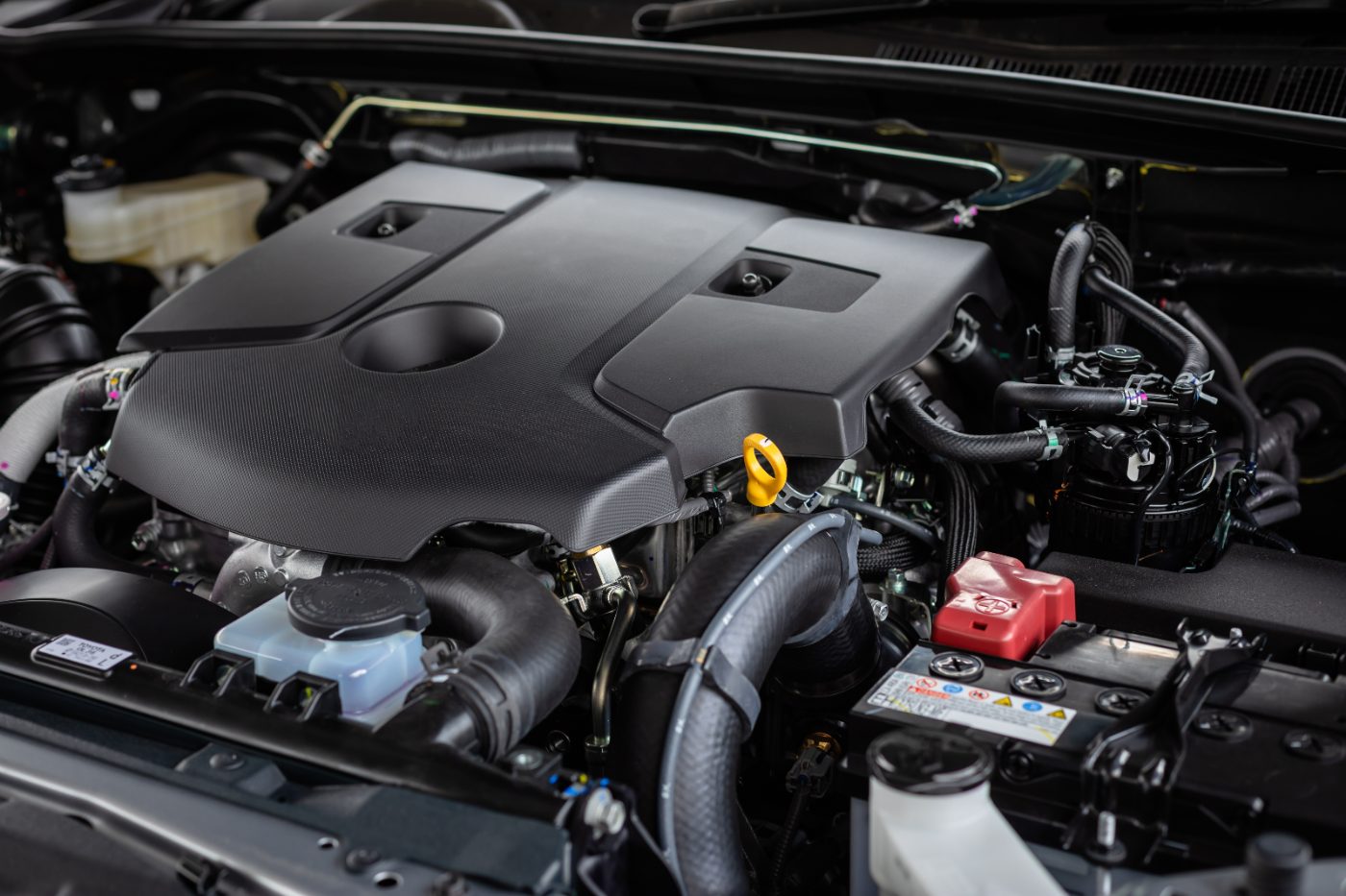 Engine bay showing carbon fiber cover, yellow dipstick, red battery terminal, and fluid reservoirs