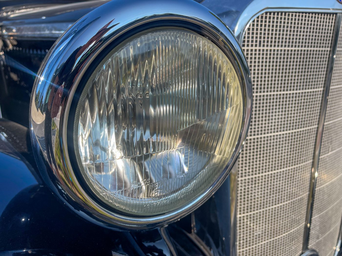 Vintage car headlight with chrome ring and ribbed glass lens next to metal mesh grille