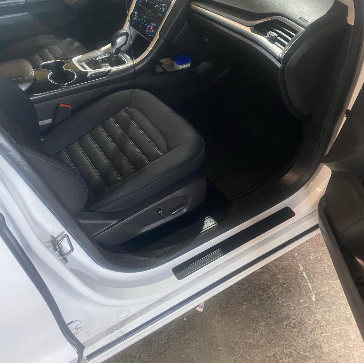 White car interior with black leather driver seat and dashboard visible through open door