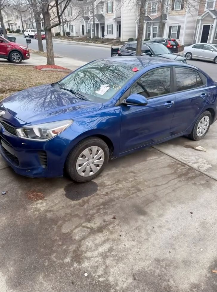 Blue Kia sedan parked on residential street with bare trees and townhouses in background