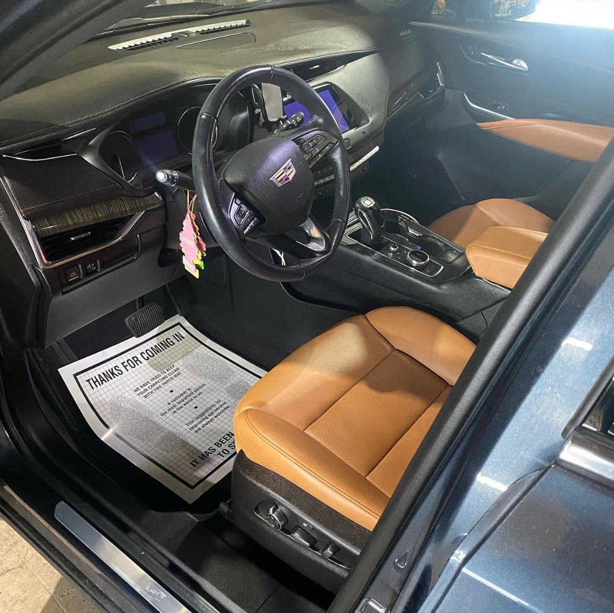 Cadillac luxury car interior with tan leather seats, black steering wheel, and digital dashboard display