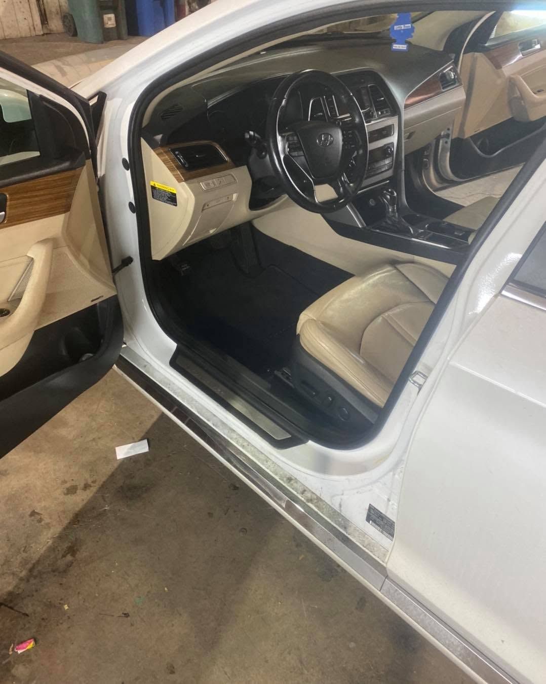 White sedan interior with cream leather seats, steering wheel, and open driver door in showroom