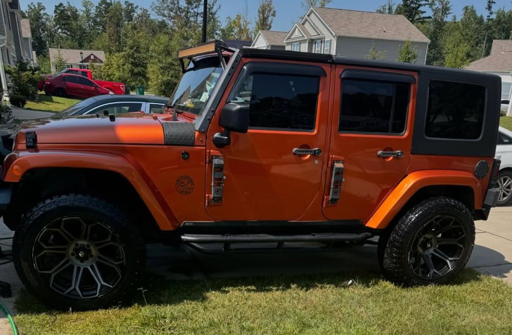 Orange Jeep Wrangler with custom wheels parked on residential driveway