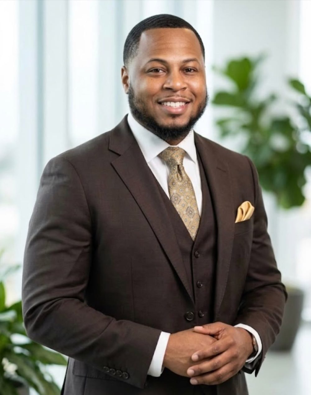 Professional man in brown suit with gold tie and pocket square smiling at camera